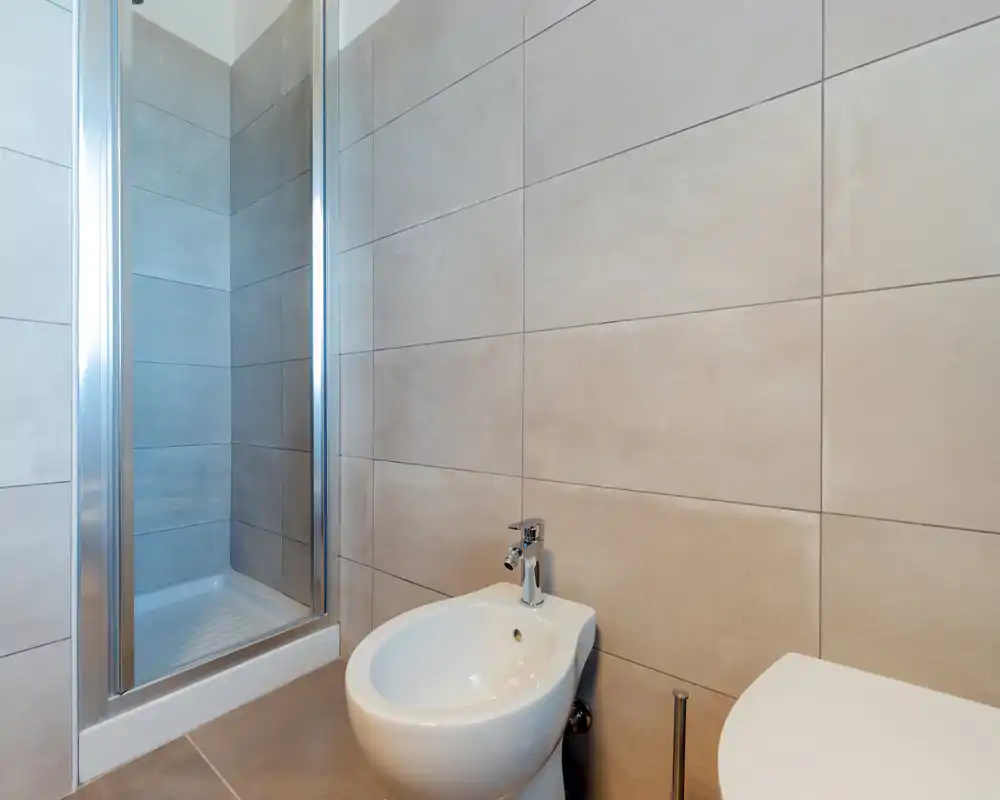 Bagno moderno con pareti piastrellate, doccia con porta in vetro e bidet e WC bianchi in primo piano.