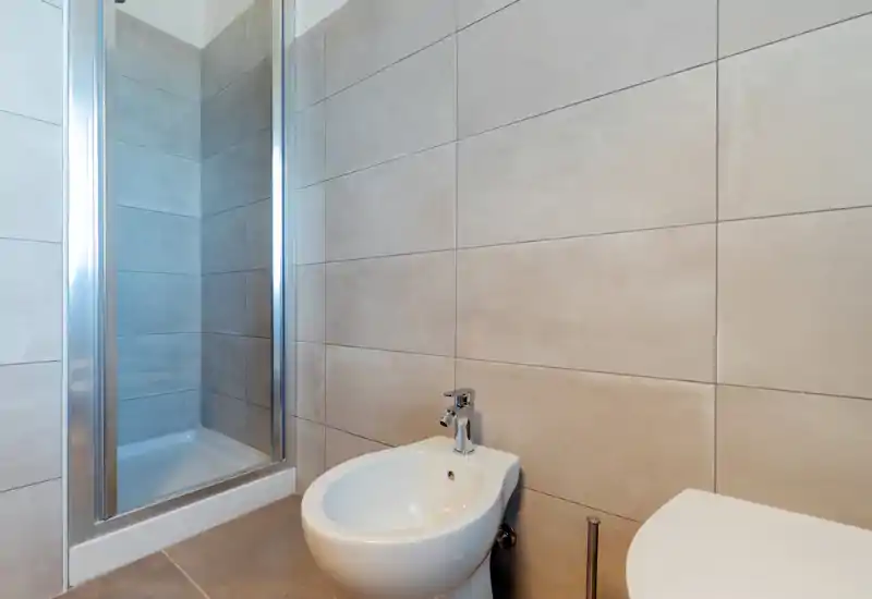 Modern bathroom with tiled walls, a walk-in shower with glass door, and a white bidet and toilet in the foreground.
