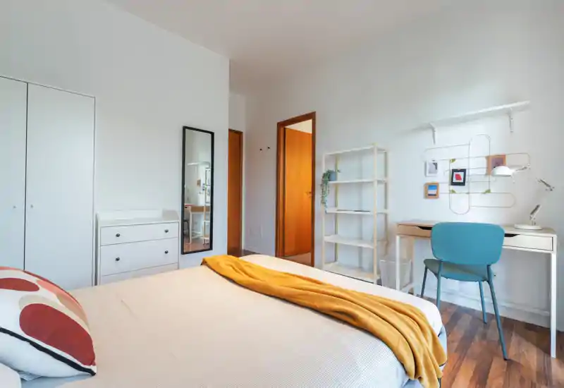 Camera da letto luminosa e moderna con letto ben rifatto, plaid color senape e un angolo scrivania funzionale — perfetta per soggiorni brevi o lunghi.