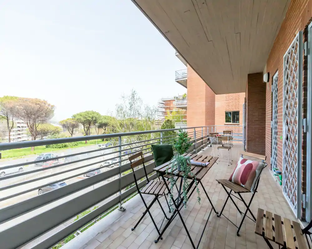 Balcone soleggiato arredato con sedie pieghevoli e un piccolo tavolo, affacciato su alberi e una strada — ideale per colazione o relax all'aperto.