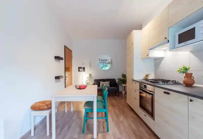Espacio diáfano luminoso y moderno con cocina compacta, mesa de comedor y un pequeño sofá — acabados en madera y detalles acogedores ideales para estancias urbanas.