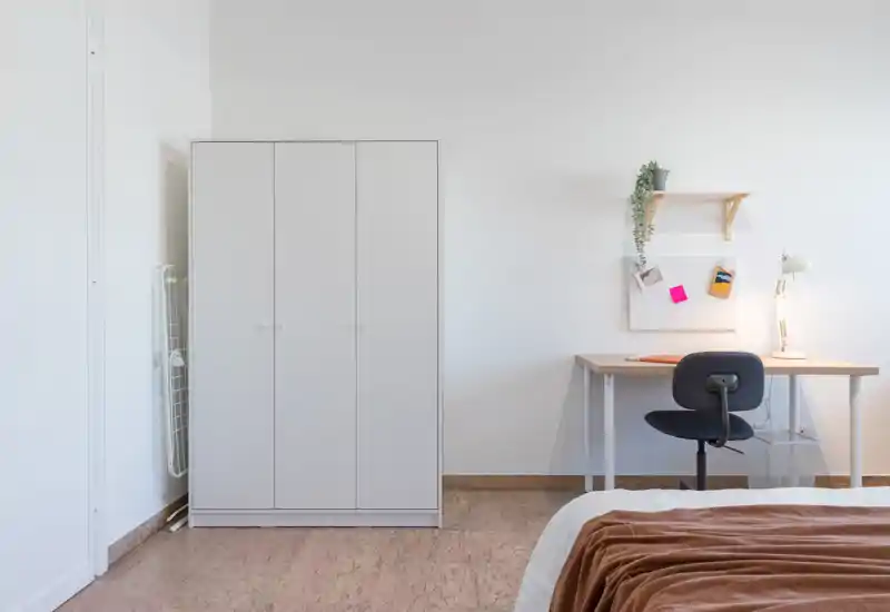 Minimal, well-lit bedroom corner with a visible bed edge, a white wardrobe and a tidy desk — bright, calm and suitable for rental photos.