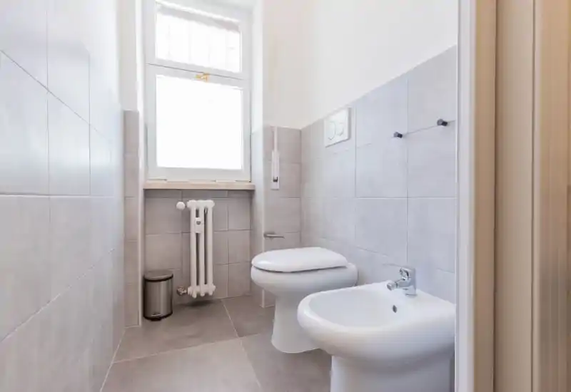 Compact, bright bathroom with toilet and bidet, tiled walls and floor, and a window providing natural light.