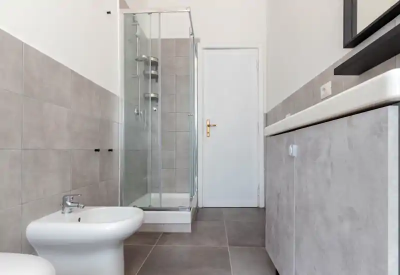Bright, modern bathroom with a tiled shower enclosure, bidet and vanity unit; neutral gray tiles and clean fixtures suit a contemporary rental.