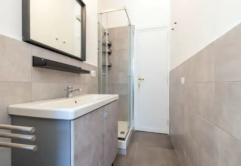 Clean, modern bathroom with a sink and enclosed shower, neutral grey tiles and simple fixtures—bright and functional.
