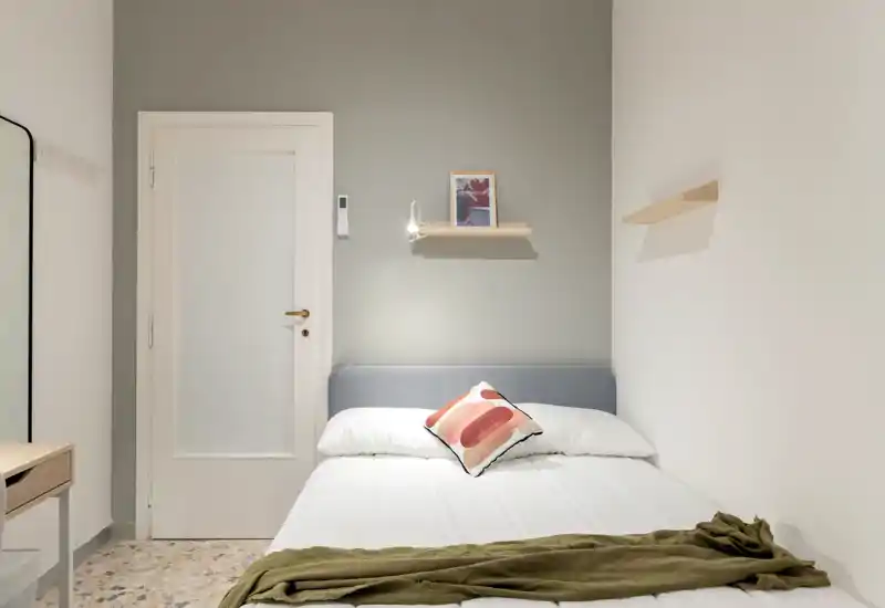 Dormitorio minimalista con cama bien hecha, cojín decorativo y luz suave de mesita; tonos neutros y líneas limpias que crean un ambiente tranquilo y luminoso.