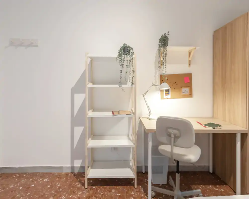 Rincón de dormitorio luminoso y minimalista con escritorio, estantería y plantas — ideal como zona de estudio en un dormitorio pequeño.