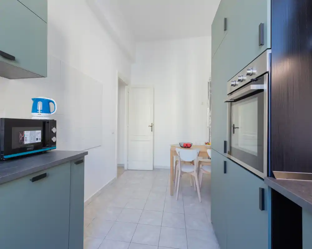 Cuisine moderne et lumineuse avec meubles vert d'eau, four encastré, micro-ondes et petite table à manger — lignes épurées et agencement fonctionnel, parfait pour de courts séjours.
