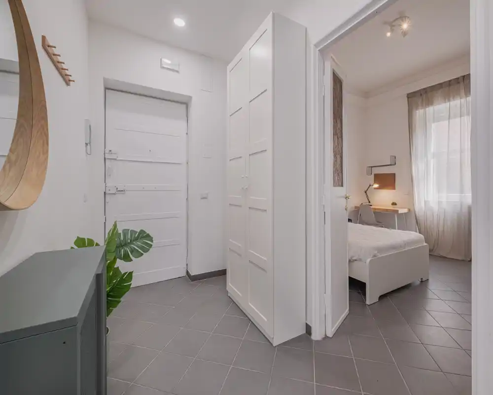 Entrada luminosa y moderna con suelo de baldosas, armario empotrado y vista a un dormitorio contiguo. Tonos neutros y decoración minimalista que crean una bienvenida agradable.