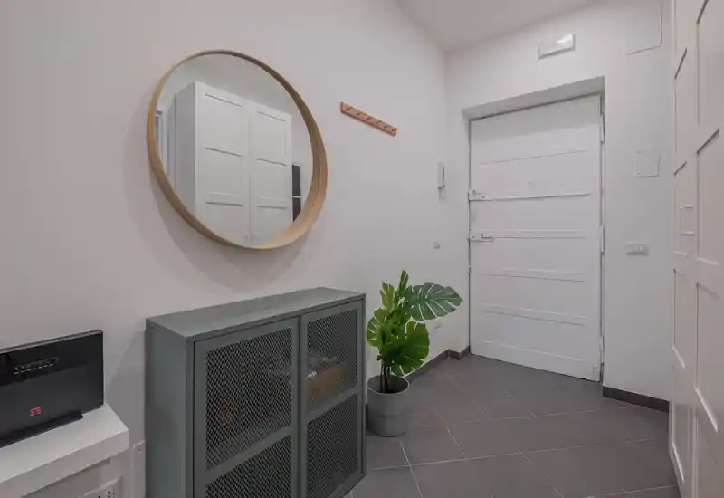 Entrée lumineuse et minimaliste avec porte blanche, grand miroir rond, petit meuble de rangement et plante en pot — une entrée soignée et accueillante.