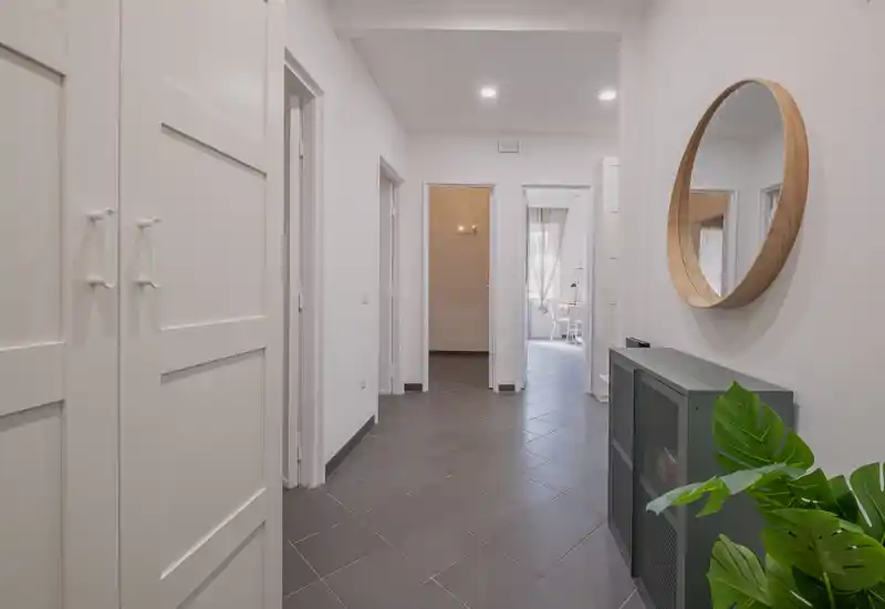 Entrée moderne et lumineuse avec sol carrelé, rangements intégrés, grand miroir rond et plante décorative — un espace d'accueil soigné.
