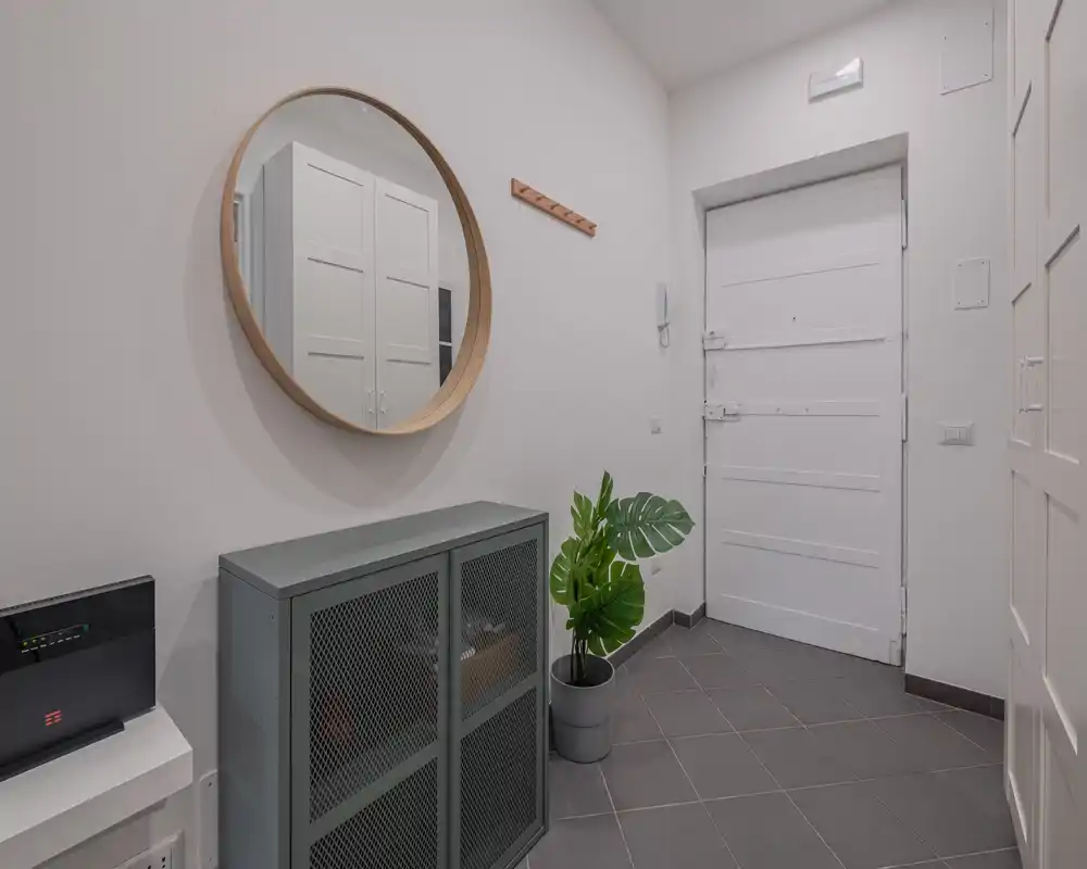 Bright, modern entryway with a white door, round wall mirror, console cabinet and a potted plant; clean minimalist styling ideal for a rental listing.