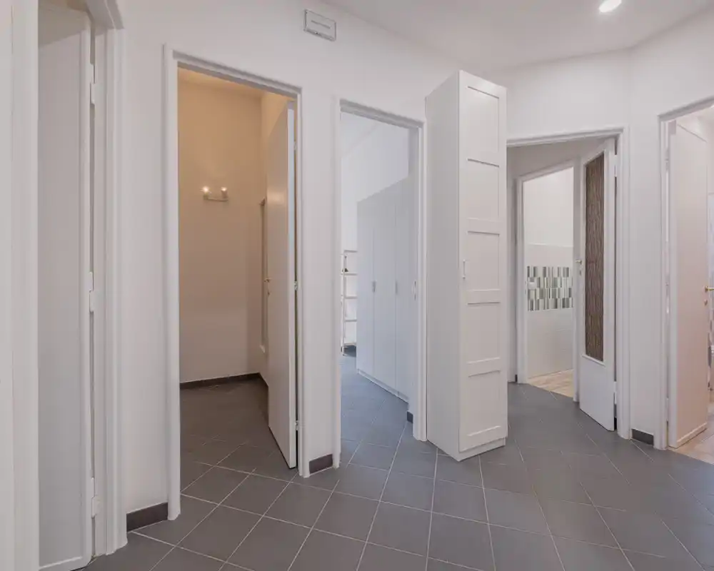 Bright, modern entrance/hallway with gray tiled floor and multiple doors leading to adjacent rooms; clean white walls and built-in storage maximize circulation space.