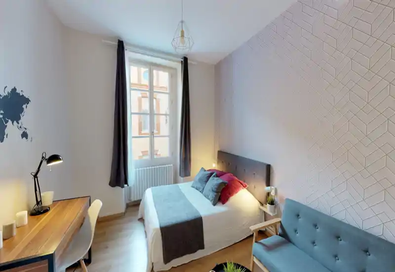 Bright, well-styled bedroom with a comfortable double bed, decorative pillows and a textured accent wall. Natural light from the window and layered lamps create a warm, welcoming atmosphere.