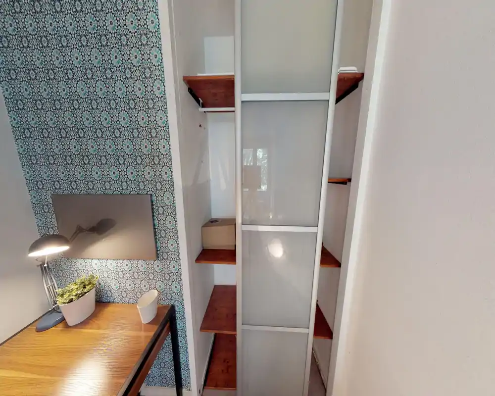 Angolo di camera con scrivania in legno, parete decorativa a fantasia, scaffali e porta scorrevole dell'armadio; il letto non è visibile in questa immagine.