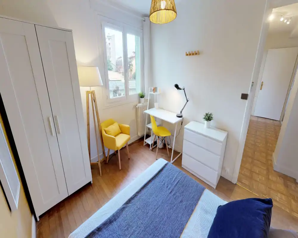 Sunny, well-staged double bedroom with a visible bed, white wardrobe, desk and cozy yellow accents. Bright natural light and clean, modern furnishings create a welcoming space for rest or work.