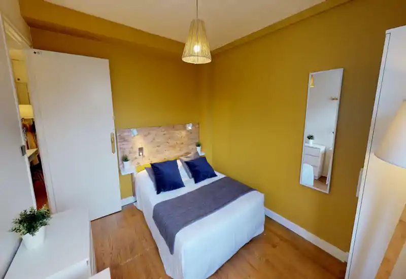 Bright, cozy bedroom with a double bed, wooden headboard and warm mustard walls; navy cushions and soft textiles create a welcoming atmosphere.