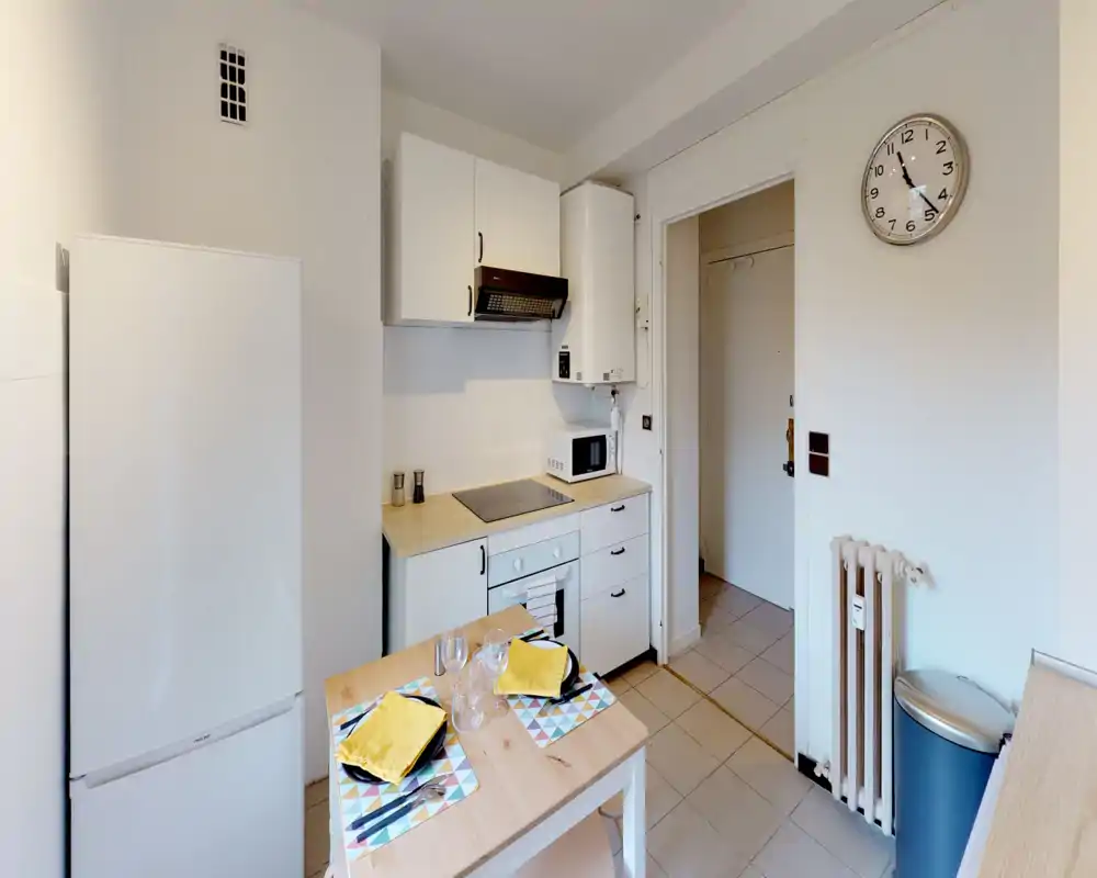 Compact, well-equipped kitchen with white cabinets, induction hob, oven, microwave and a small dining table set for two. Bright, tidy and efficiently arranged — ideal for a short-stay or city apartment.