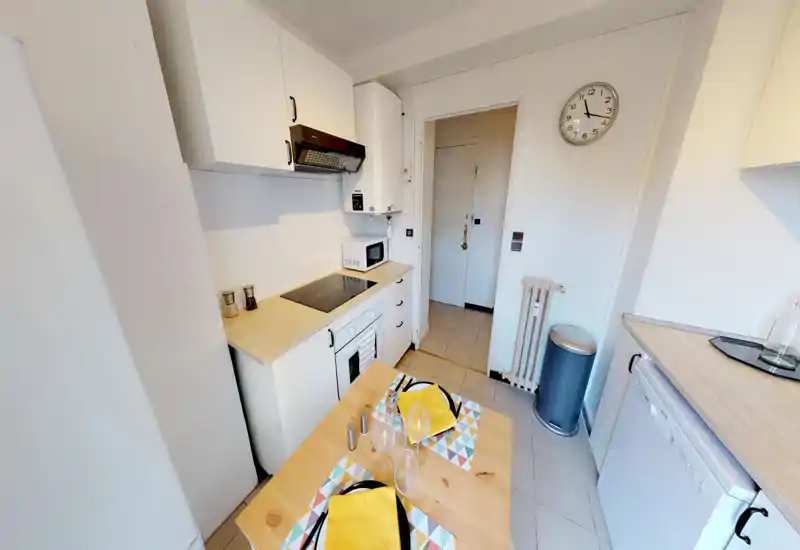 Compact, well-equipped kitchen with light wood countertops, induction hob, small oven and a set table for two — bright and tidy space ideal for short stays.