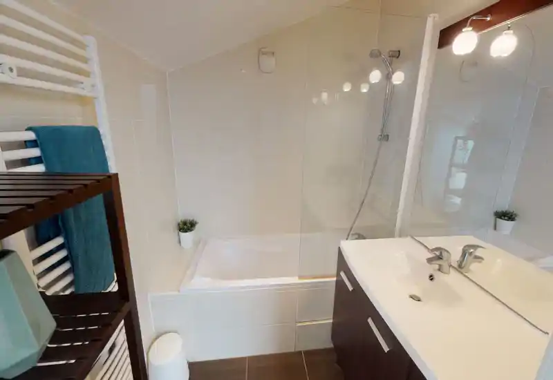Salle de bains lumineuse et soignée avec baignoire-douche, radiateur porte-serviettes mural et meuble lavabo contemporain avec miroir.