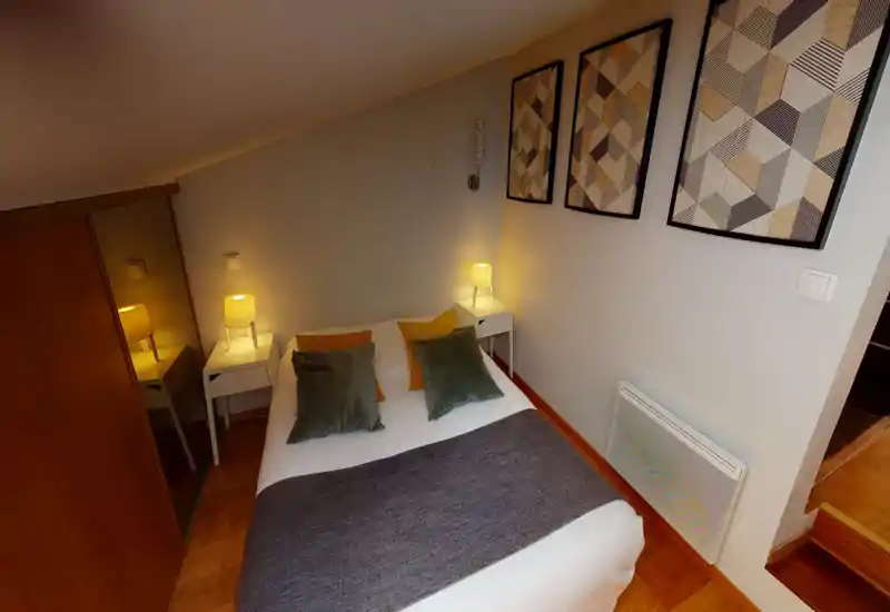 Chambre compacte et bien décorée avec lit double, tables de chevet et lampes chaudes; coussins et tableaux apportent une ambiance cosy.