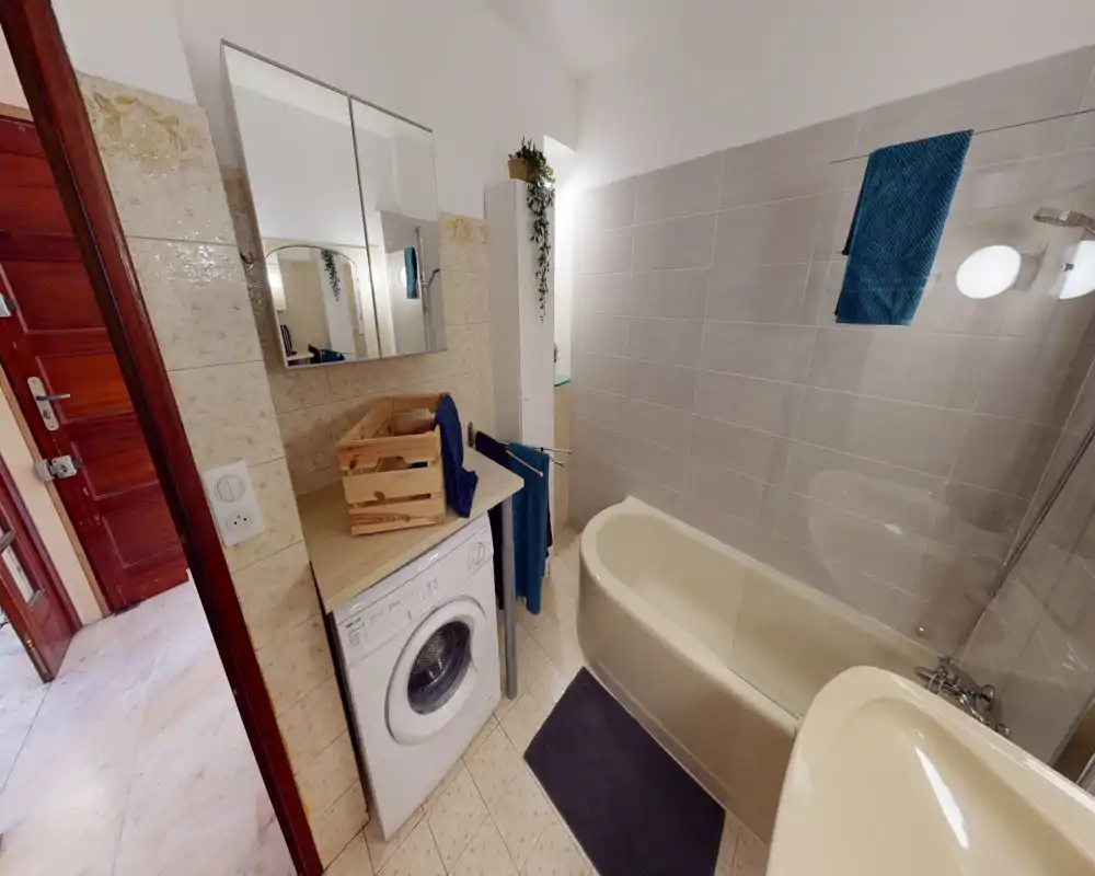 Bright, well-kept bathroom with a bathtub, shower screen, sink and a washing machine tucked under the counter; neutral tiles and teal accents give a fresh feel.