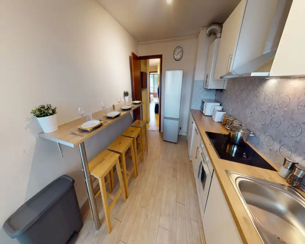 Bright, modern galley kitchen with wooden countertops, built-in stove and sink, plus a breakfast bar with stools — tidy and well staged for a rental listing.