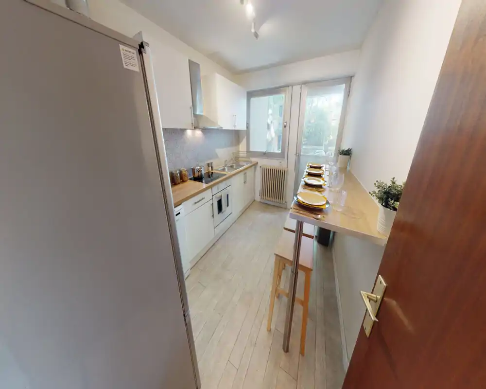 Bright, modern galley kitchen with white cabinets, wooden countertops, integrated appliances and a breakfast bar set for four — ideal for compact urban living.