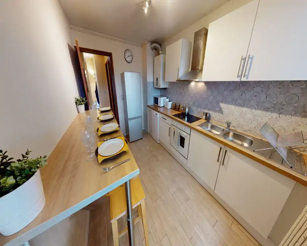 Modern, well-equipped galley kitchen with wooden countertops, integrated oven and double sink. A breakfast bar set with plates and glasses makes it ideal for casual meals.