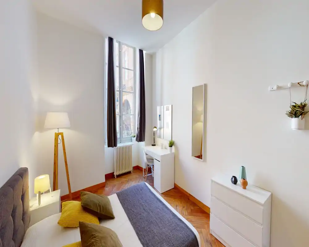 Bright, well-styled bedroom with a comfortable double bed, warm bedside lamps and a desk by a tall window that fills the room with natural light.