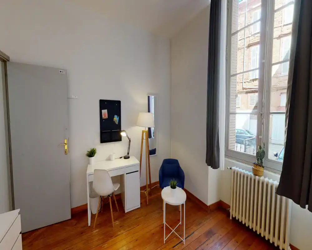 Coin salon lumineux et bien mis en scène avec bureau, fauteuil bleu et grande fenêtre laissant entrer la lumière naturelle ; parquet et décor minimaliste pour une atmosphère chaleureuse.