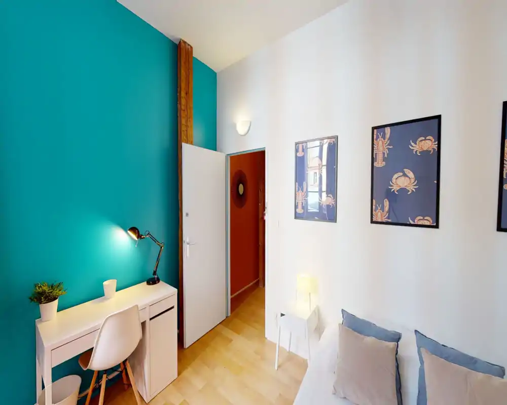 Chambre lumineuse et élégante avec un mur d'accent turquoise, lit confortable avec coussins, table de chevet et un petit bureau — idéale pour se détendre ou travailler.