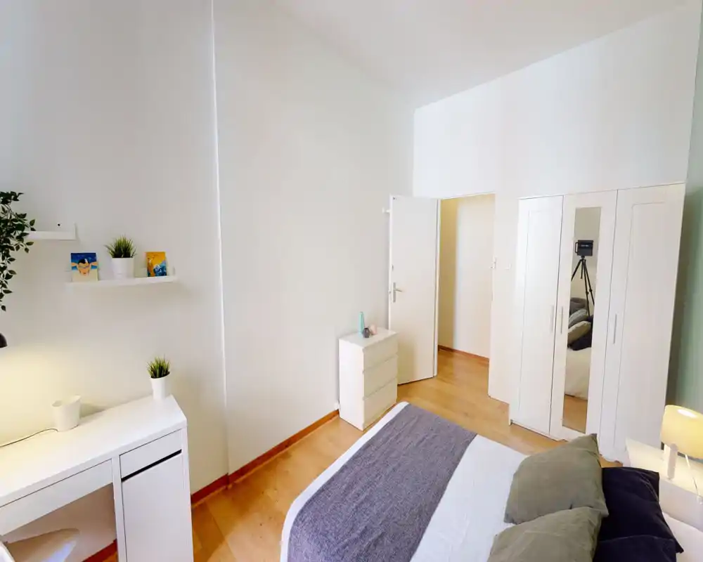 Bright, minimal bedroom with a neatly made double bed, bedside lamp, wardrobe with mirror and simple white furniture—comfortable and modern styling ideal for listings.