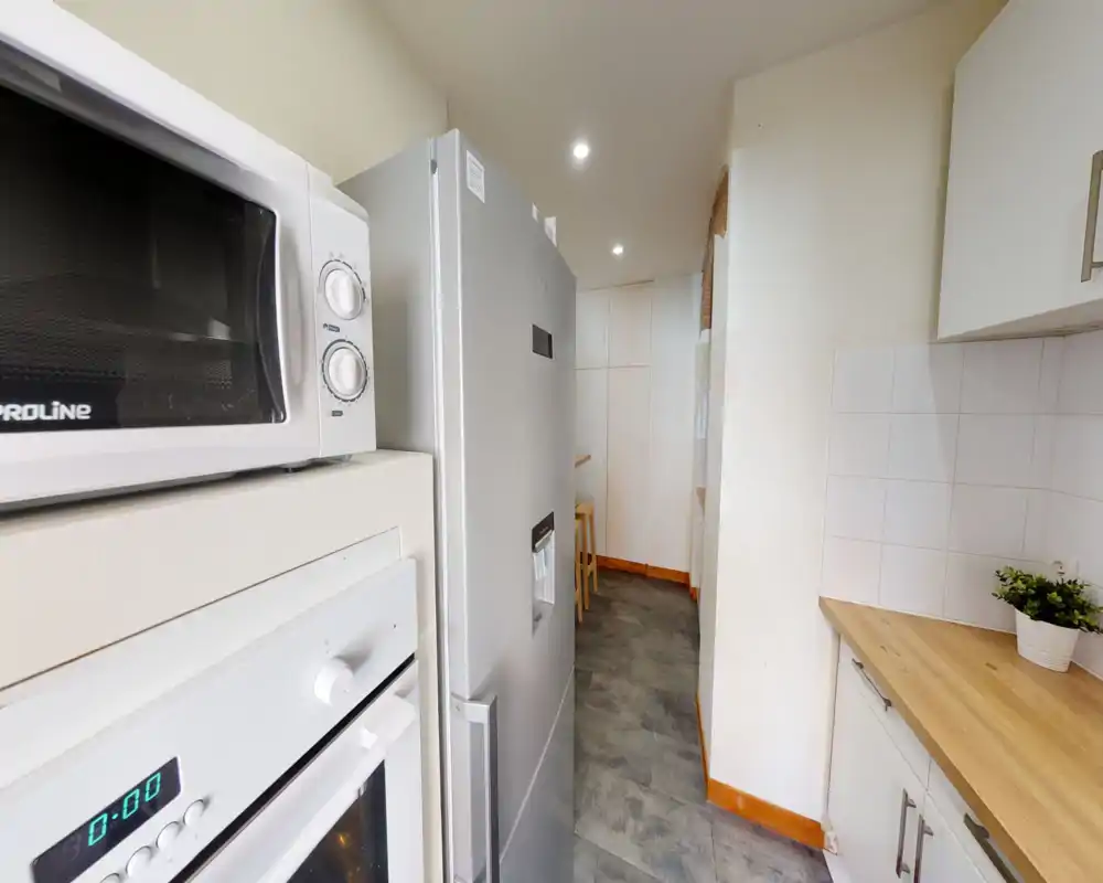 Cuisine en enfilade moderne avec réfrigérateur en inox, four encastré et plan de travail en bois. Espace lumineux et rangé, parfait pour un appartement compact.