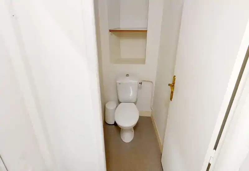 Bagno di servizio compatto con WC a cisterna attaccata, piccolo cestino e mensola incassata sopra. Pareti neutre e pavimento pratico lo rendono un bagno funzionale per gli ospiti.