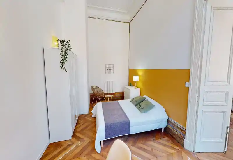 Chambre lumineuse et stylée avec lit double, mur d'accent moutarde, parquet et rangement minimaliste — un espace cosy et bien éclairé, idéal pour les courts séjours.