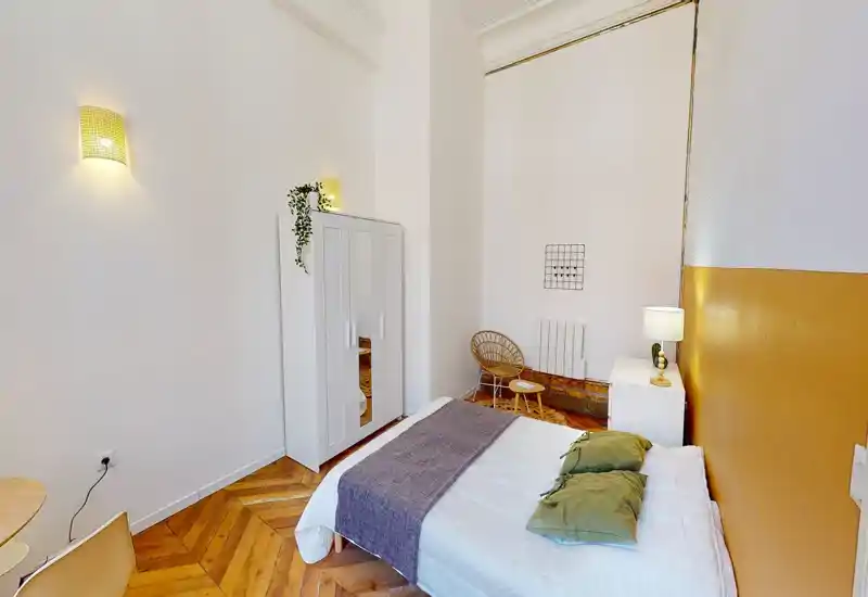 Chambre lumineuse et bien mise en scène avec lit double, table de chevet et armoire ; parquet chaleureux et textiles doux pour une ambiance accueillante.