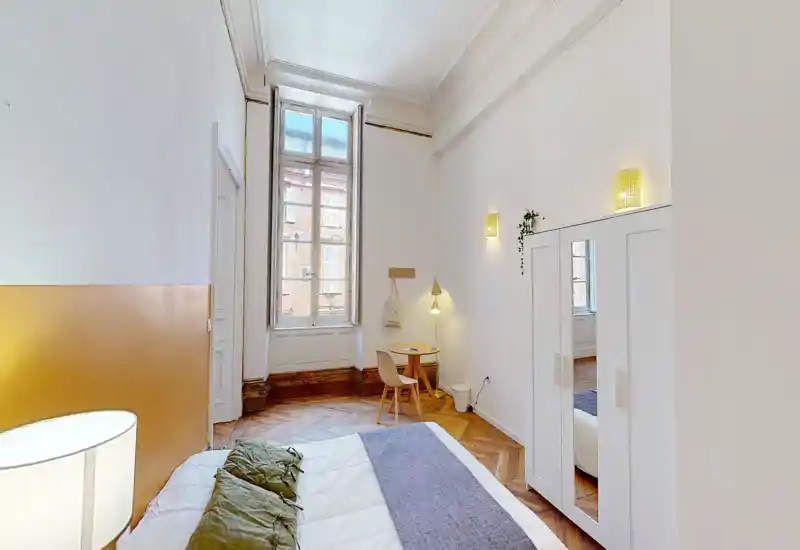Chambre lumineuse et élégante avec une grande fenêtre, parquet en point de Hongrie et un lit double confortable habillé de linges neutres.
