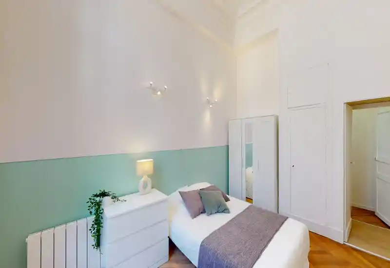 Camera da letto singola luminosa e ariosa con un letto confortevole, cuscini e una piccola cabina armadio. Parete verde menta e pavimento in legno donano un’atmosfera tranquilla e di design perfetta per affitti.
