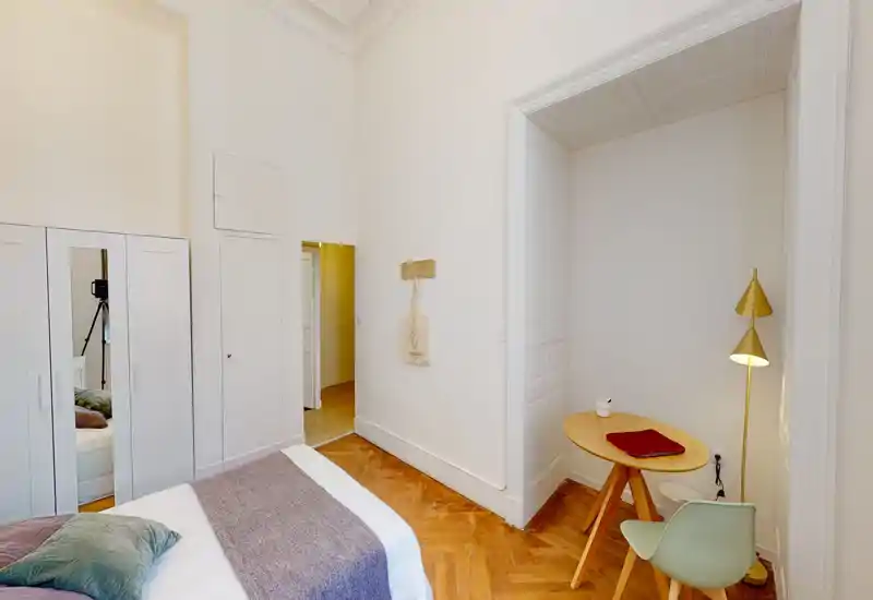 Camera da letto luminosa e curata con letto matrimoniale, tessili accoglienti e un piccolo angolo lavoro su pavimento in parquet caldo — perfetta per soggiorni confortevoli.