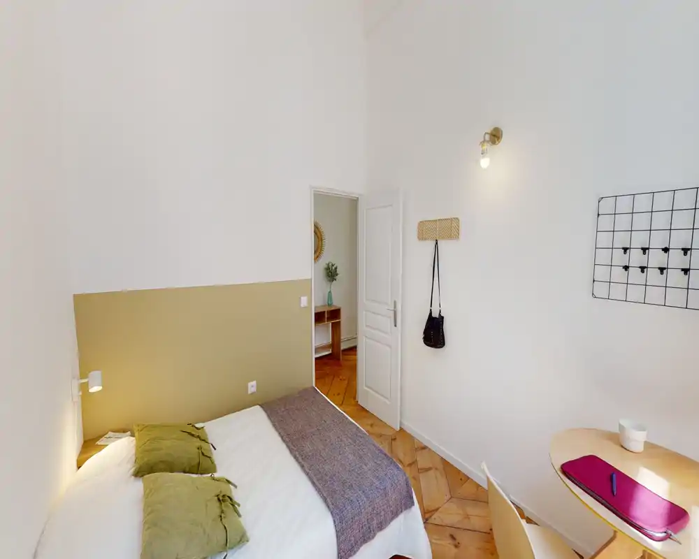 Chambre lumineuse et chaleureuse avec un lit double confortable, coussins vert olive et parquet chaleureux; petit bureau mural pour travailler ou prendre un café.