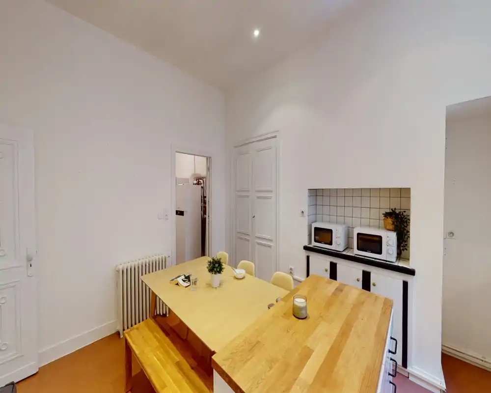Coin repas lumineux et moderne avec une grande table en bois et une banquette, plan de travail avec petits appareils ; tons chauds et décor sobre pour une ambiance accueillante.