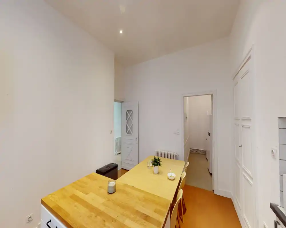 Coin repas lumineux et épuré avec table en bois, chaises et décoration minimale ; murs blancs et sol chaud offrent un espace propre et accueillant.