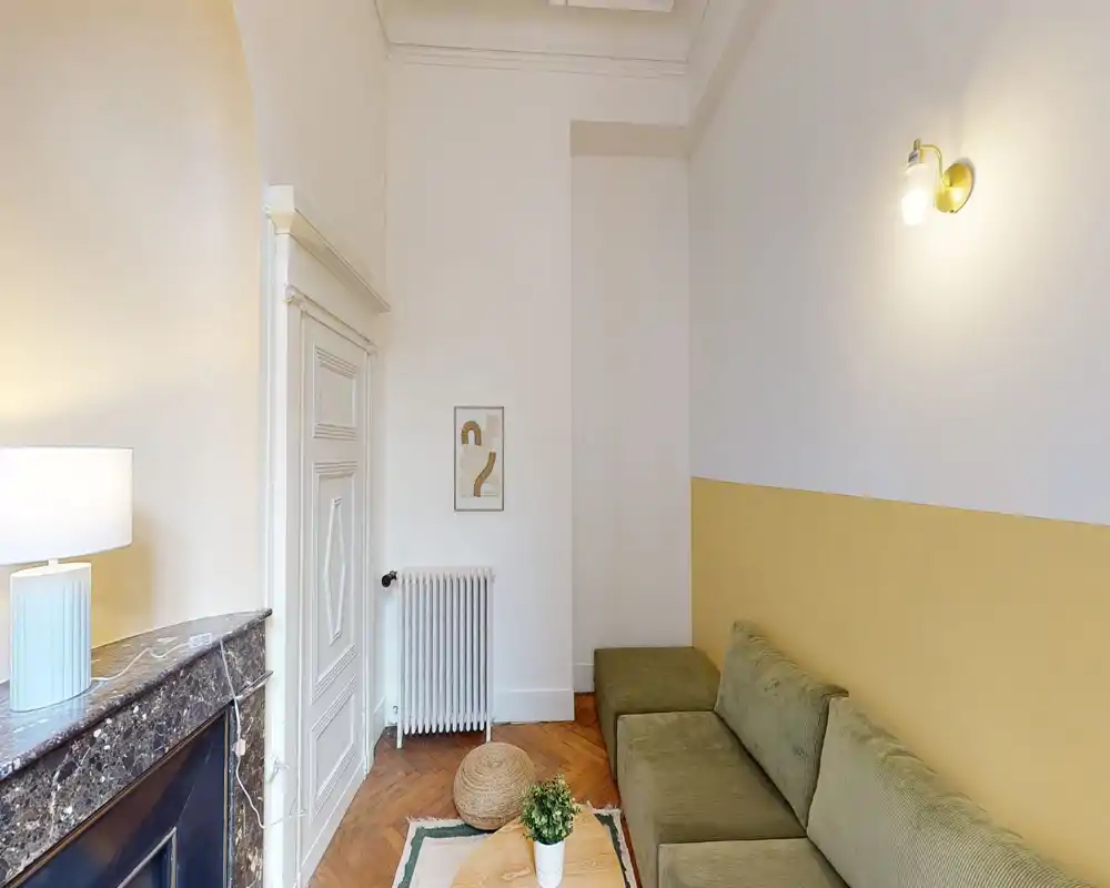 Coin salon lumineux et bien décoré avec un canapé vert, tapis décoratif et petite table basse ; des tons chauds et neutres créent une atmosphère cosy et moderne.