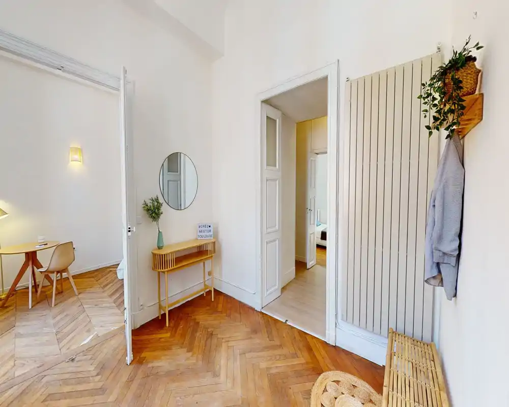 Entrée lumineuse et soignée avec parquet en chevrons, petite console, miroir mural et patères — espace de transition accueillant.
