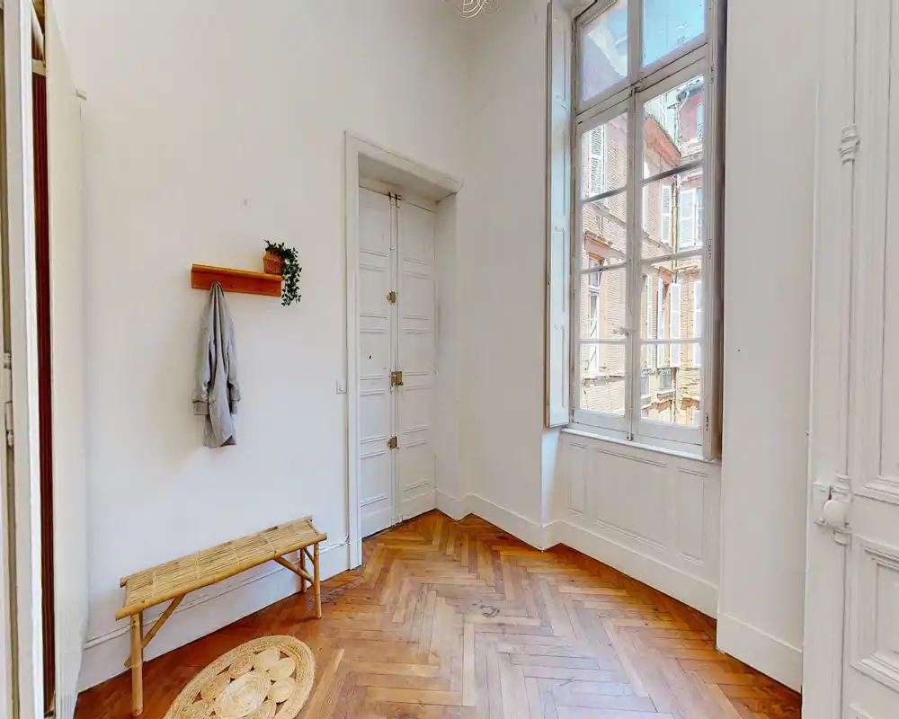 Entrée lumineuse et élégante avec parquet en chevrons, un banc et une grande fenêtre apportant de la lumière naturelle — idéale comme hall d'accueil.