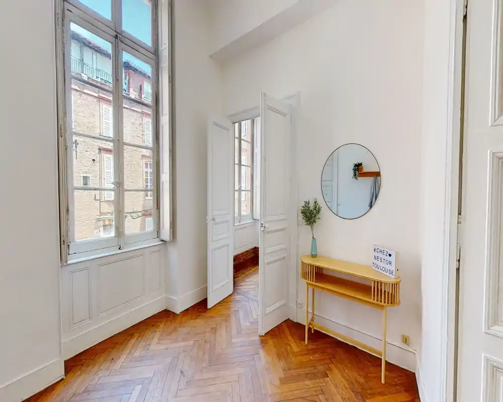 Entrée lumineuse avec grandes fenêtres, parquet en chevrons et une petite console avec miroir — première impression élégante.