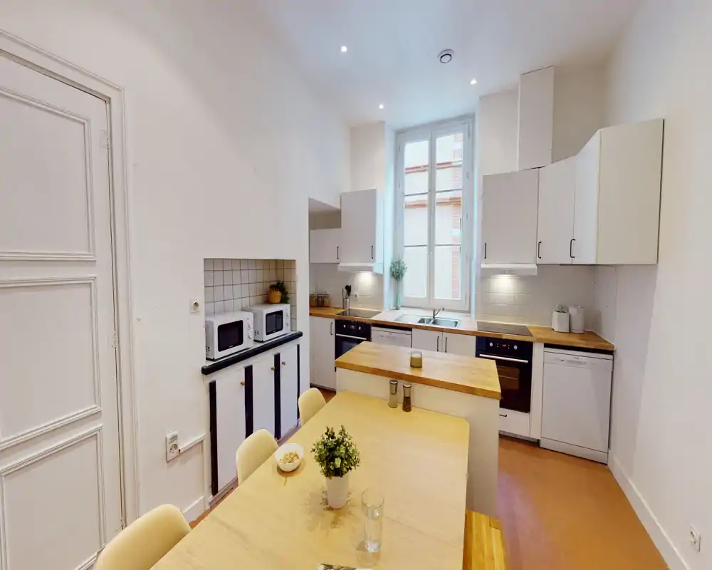 Cuisine moderne et lumineuse avec plans de travail en bois, électroménagers intégrés et table centrale — bien mise en scène pour une annonce locative.