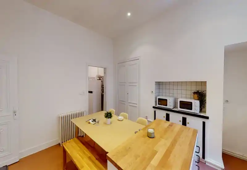 Zona pranzo luminosa e moderna con grande tavolo e panca in legno, piano con piccoli elettrodomestici; toni caldi e arredo semplice per un ambiente accogliente.