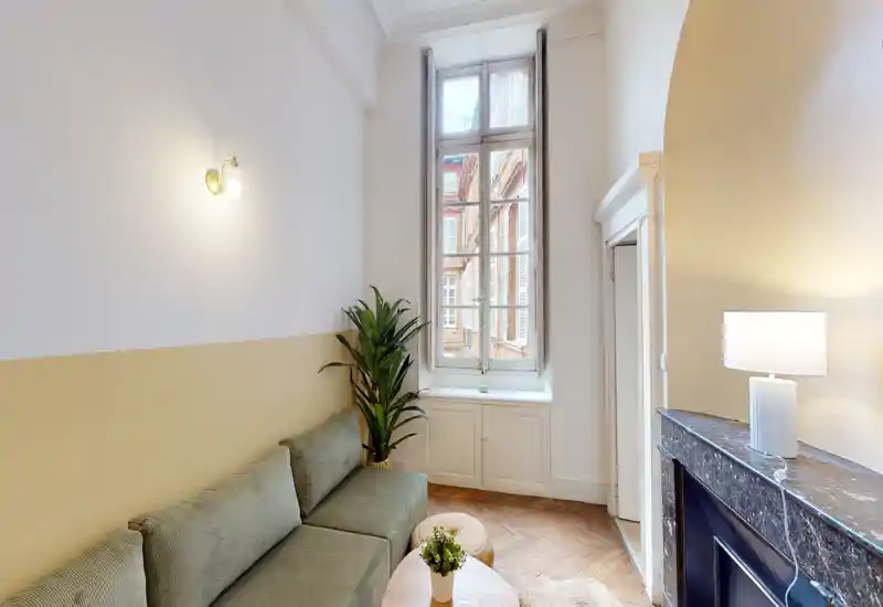 Salon lumineux et élégant avec canapé vert, grande fenêtre et cheminée décorative — coin cosy avec plantes et éclairage doux.